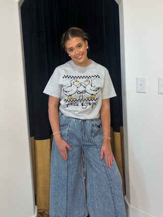 Person wearing a graphic t-shirt and jeans standing in a room with dark curtains.