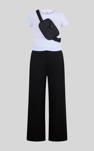 A child's outfit consisting of a white short-sleeve t-shirt, black wide-leg pants, and a black crossbody fanny pack, displayed on a neutral gray background.