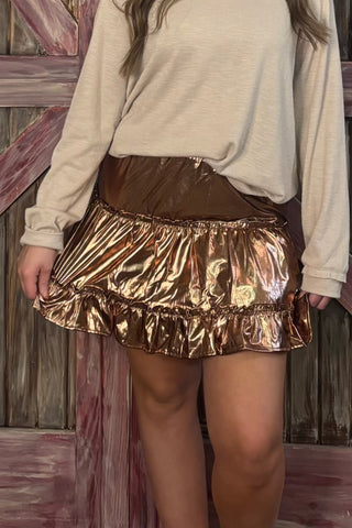 Person wearing a gold metallic skirt with a beige sweater against a wooden background