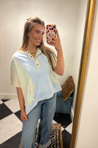 Woman taking a mirror selfie wearing a light blue top and jeans in a room with a checkered floor.