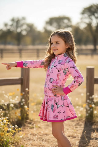 Young girl in a pink dress with cowgirl print standing in a field.