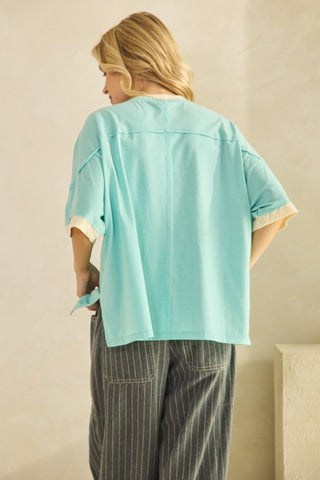 Person wearing a light blue oversized shirt and striped pants against a beige wall.
