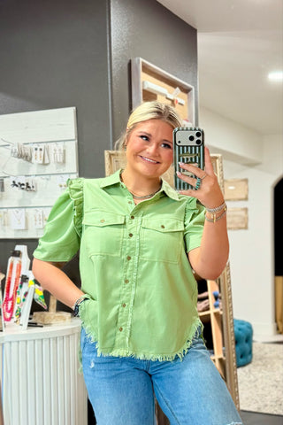 Woman taking a mirror selfie wearing a green denim shirt and blue jeans in an indoor setting.