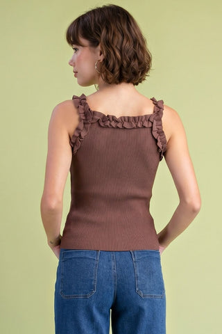 A woman shown from the back wearing a ribbed brown sleeveless top with ruffled shoulder straps, paired with blue jeans, against a solid pale yellow-green background.