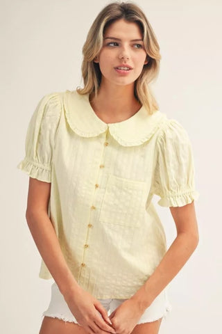 Woman wearing a light yellow blouse with a collar on a plain background