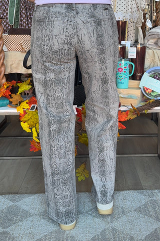 Gray and black snakeskin print wide-leg pants shown from the back on a model, standing in a retail store setting.