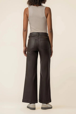 A model shown from the back wearing dark brown wide-leg pants, a light beige ribbed tank top, and gray slip-on shoes, set against a plain cream studio background.