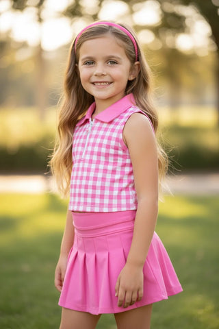 Young girl in a pink checkered top and skirt standing outdoors with a blurred natural background