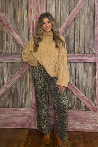 Woman wearing a beige sweater and leopard print pants standing in front of wooden doors.