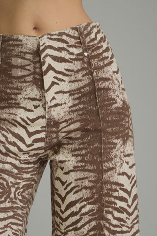 Close-up of a person wearing high-waisted trousers with a brown and beige zebra-like animal print, shown against a plain gray studio background.
