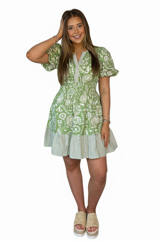 Woman wearing a green floral dress against a white wall