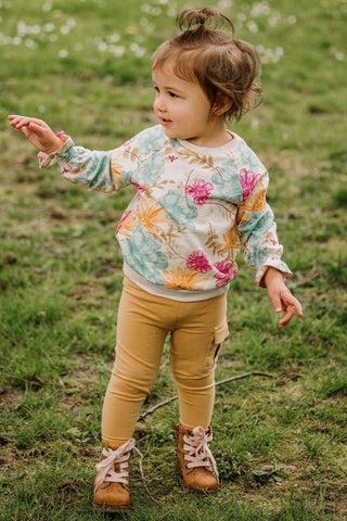 Child wearing a floral sweater and yellow pants standing in a grassy field