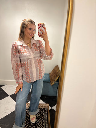 Woman taking a mirror selfie wearing a patterned blouse and jeans.