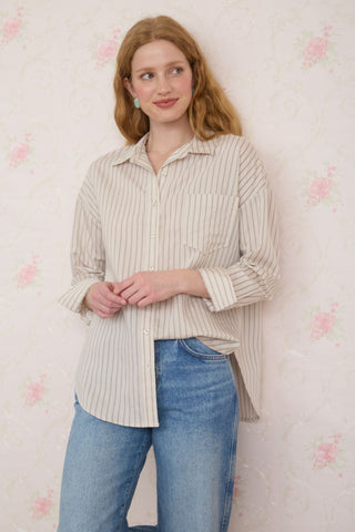 Woman wearing a striped shirt and jeans against a floral wallpaper background