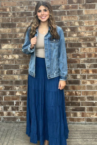 Woman wearing a denim jacket and blue skirt against a brick wall
