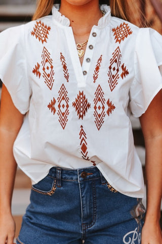White blouse with red geometric patterns worn by a person, with a blurred background.