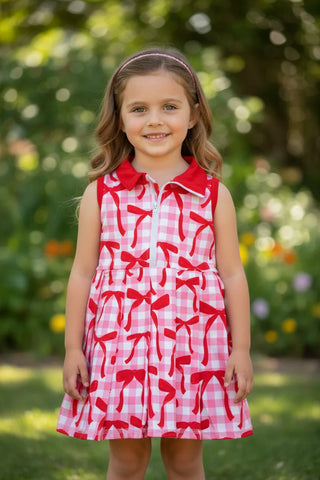 Young girl wearing a red and white checkered dress with bow pattern outdoors.