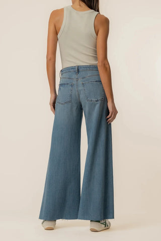 Person wearing a light green sleeveless top and blue wide-leg jeans on a beige background
