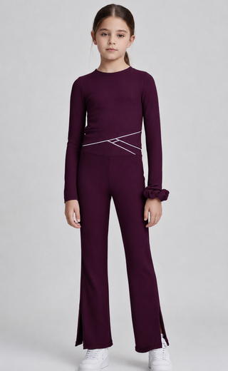 A young girl modeling a matching deep maroon long-sleeve top and wide-leg pants set with white geometric line details on the waist, photographed against a neutral light gray background.