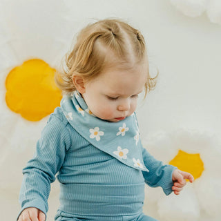 Child wearing a blue outfit with a floral bib, standing against a neutral background.