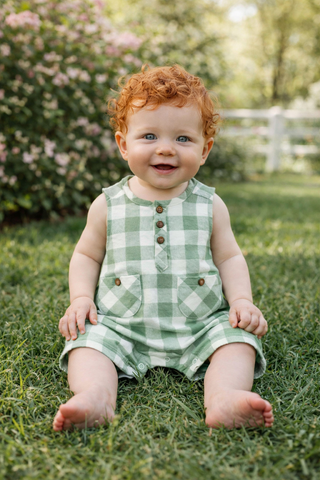 baby wearing green check romper in a yard