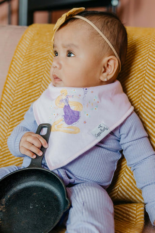 Baby holding a small black pan with a colorful bib featuring a mermaid design.