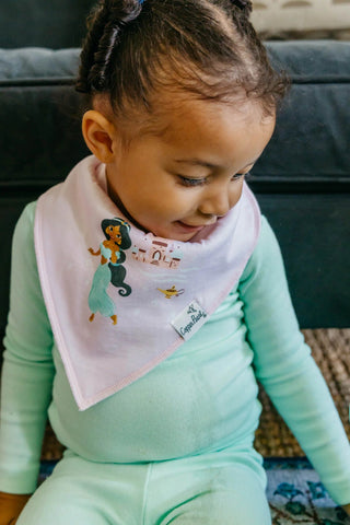 Child wearing a bib with cartoon character and holding a green toy, sitting on a couch.