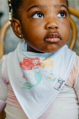 Child wearing a bib with mermaid design and visible brand name.