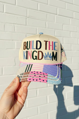 Cap with 'Build the Kingdom' text held against a white brick wall