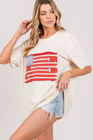 Woman wearing a white oversized shirt with an American flag design on a plain background