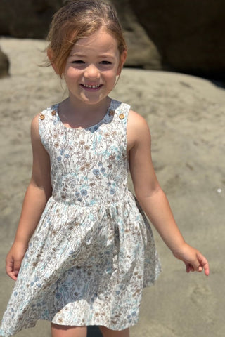 Young girl in a floral dress standing on a rocky beach.