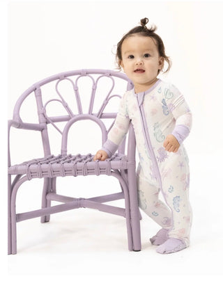 Child in a white outfit with purple accents standing next to a small purple chair on a white background