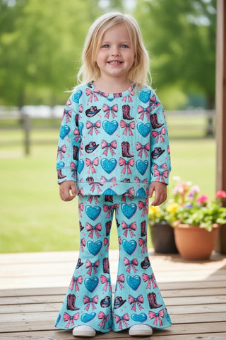 Child wearing a colorful pants set with bows and hearts on a wooden deck.