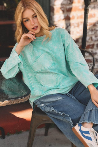 Woman wearing a teal sweater and blue jeans sitting outdoors.