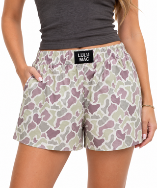 A model wearing Lulu Mac camouflage print shorts with a gray crop top, shown from the chest down against a white background.