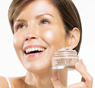 Woman holding a jar of 'Champagne Moon Dirt' facial mousse against a white background