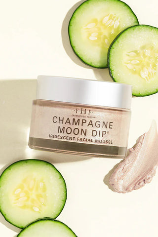 Facial mousse jar labeled 'Champagne Moon Dip' with sliced cucumbers on a light background