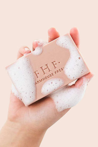 A hand holding a rectangular bar of soap covered in white foam, with the brand name 'FHF. ARMAHOUSE FREE' printed on the front, against a soft pale pink background.