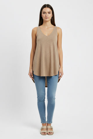 Woman wearing a beige sleeveless top and blue jeans on a white background