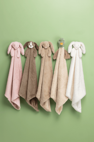 Five plush bunny-shaped baby towels in pink, taupe, beige, and white hang on a light green wall. Two of the towels have dog faces, and one has a small bird face.