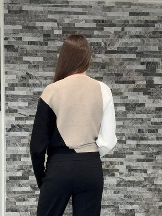 A woman viewed from behind wearing a black and white color-block vest, black pants, and beige platform sneakers, standing in a hallway with a gray stone-tile accent wall and a black-and-white checkered floor.