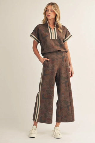 Woman wearing a brown patterned outfit with white accents on a plain background