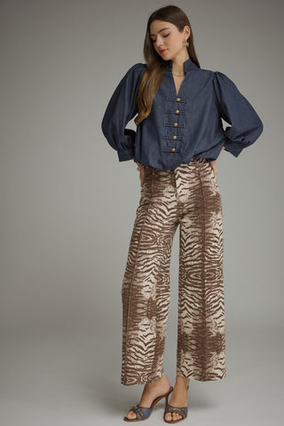 A woman modeling a navy blue button-front blouse with voluminous sleeves and wide-leg brown-and-beige zebra-print pants against a plain gray studio background.