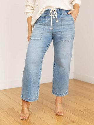 Person wearing light blue jeans on a wooden floor with a white wall background