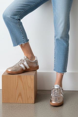 Person wearing light brown sneakers with white stripes on a plain background