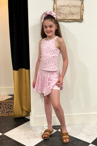Young girl in a pink polka dot outfit standing in a room with a checkered floor.