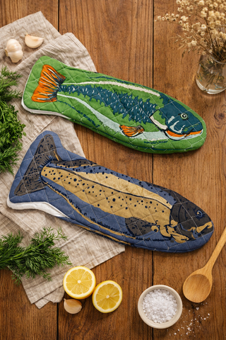 Two fish-shaped potholders on a wooden surface with lemons and herbs.