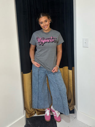 Person wearing a gray t-shirt with 'Majmada' text, blue jeans, and pink shoes in a room.