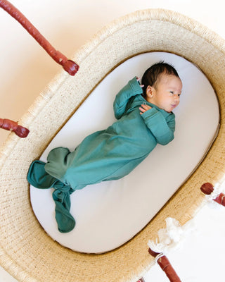 Baby in a teal onesie lying on a woven basket with a white background