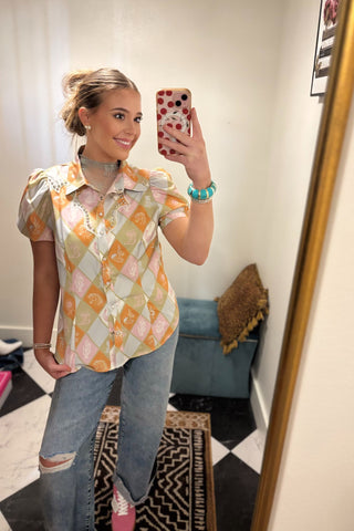 Person taking a mirror selfie wearing a patterned shirt and jeans in a room with a checkered floor.